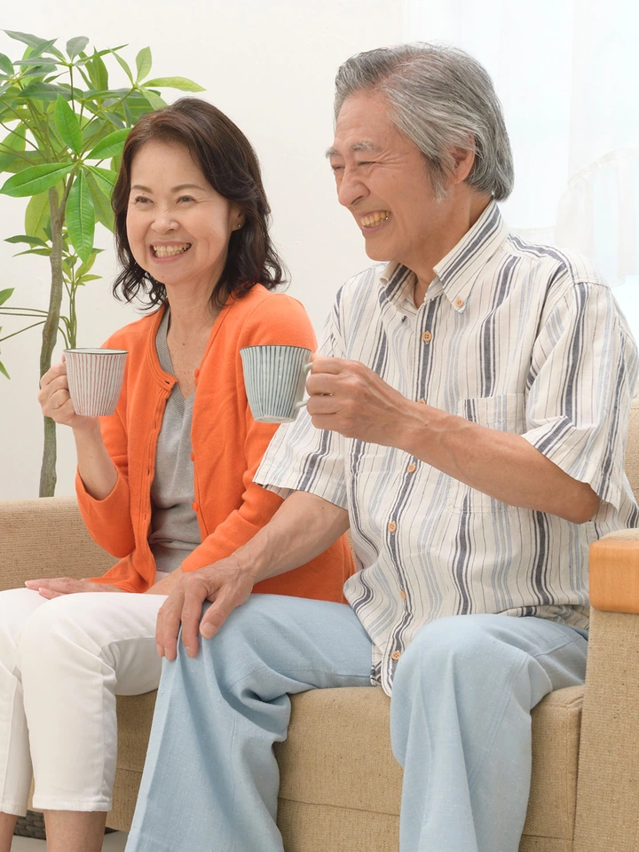 ソファで湯のみを手に談笑するシニアの夫婦